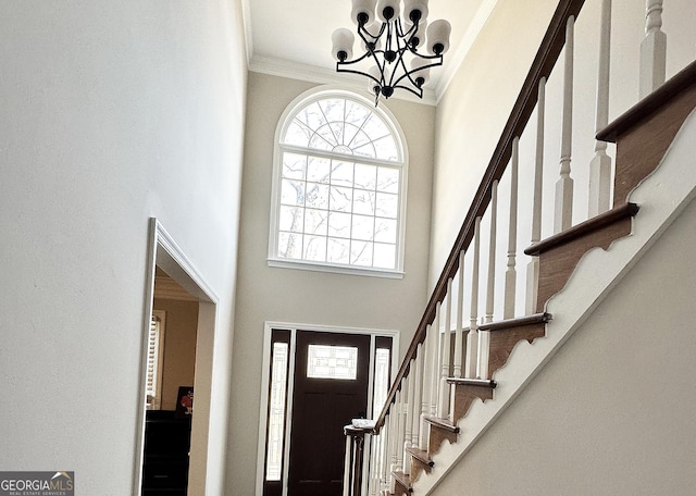 entryway featuring stairs, a notable chandelier, a towering ceiling, and crown molding