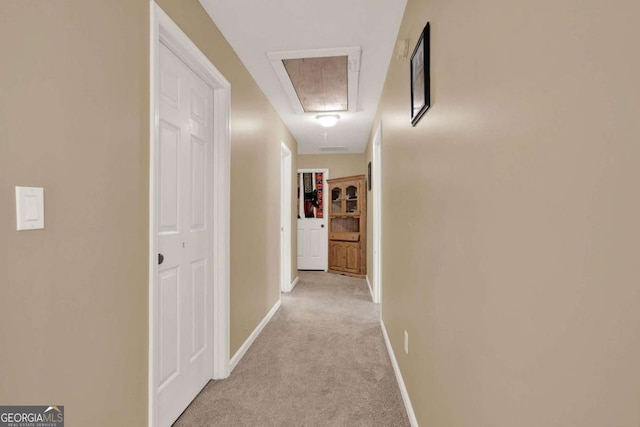 corridor featuring attic access, baseboards, and light carpet