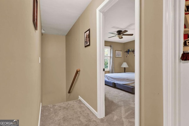 hall featuring carpet flooring, an upstairs landing, and baseboards