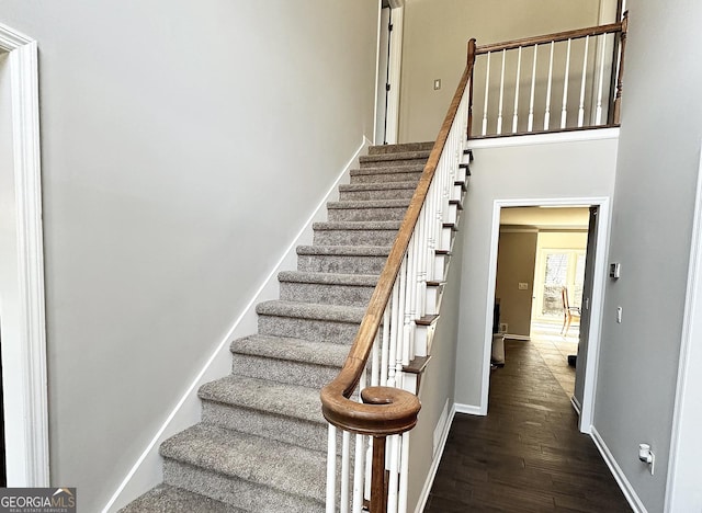 stairway featuring a high ceiling, wood finished floors, and baseboards