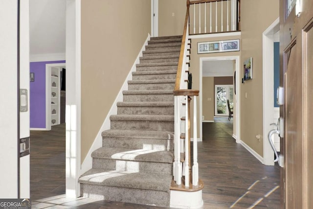 stairs with a towering ceiling, baseboards, wood finished floors, and crown molding