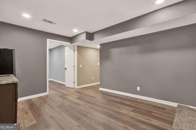 below grade area featuring visible vents, wood finished floors, freestanding refrigerator, recessed lighting, and baseboards