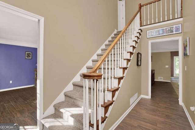 stairway with visible vents, a high ceiling, baseboards, and wood finished floors