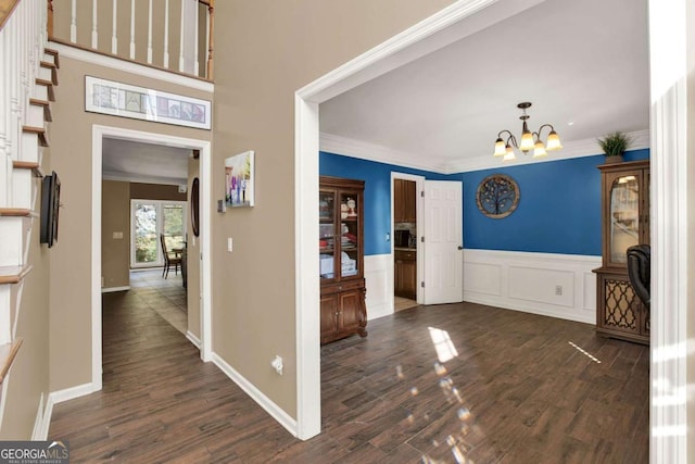 entrance foyer with a wainscoted wall, crown molding, dark wood-style flooring, and a chandelier