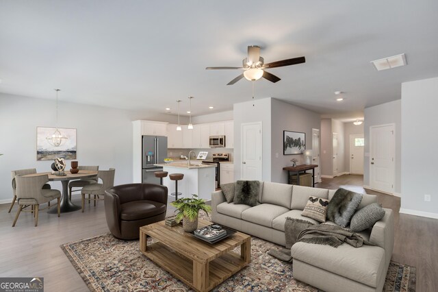 living room featuring ceiling fan with notable chandelier, light wood-type flooring, and sink