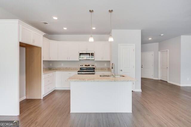 kitchen with sink, stainless steel appliances, light hardwood / wood-style floors, decorative light fixtures, and a kitchen island with sink