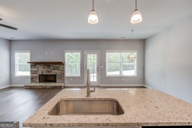 kitchen with dark hardwood / wood-style flooring, light stone counters, hanging light fixtures, and sink