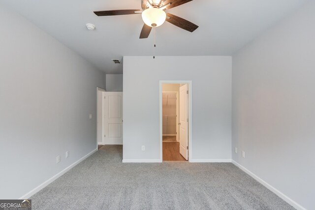 unfurnished bedroom with a spacious closet, a closet, ceiling fan, and light colored carpet