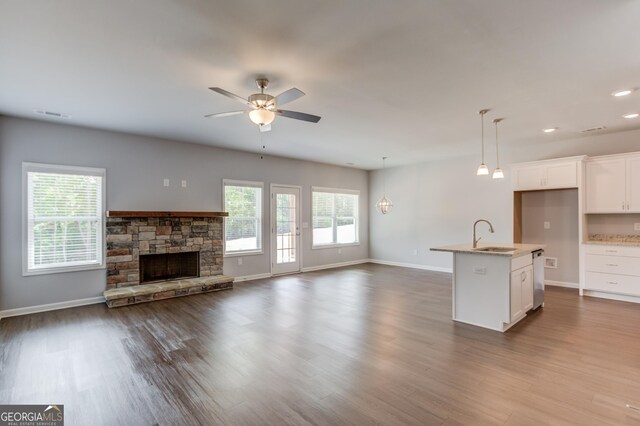 kitchen with white cabinetry, a stone fireplace, decorative light fixtures, a kitchen island with sink, and hardwood / wood-style flooring