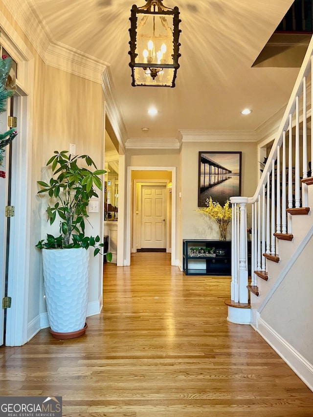 foyer entrance featuring hardwood / wood-style floors, ornamental molding, and an inviting chandelier