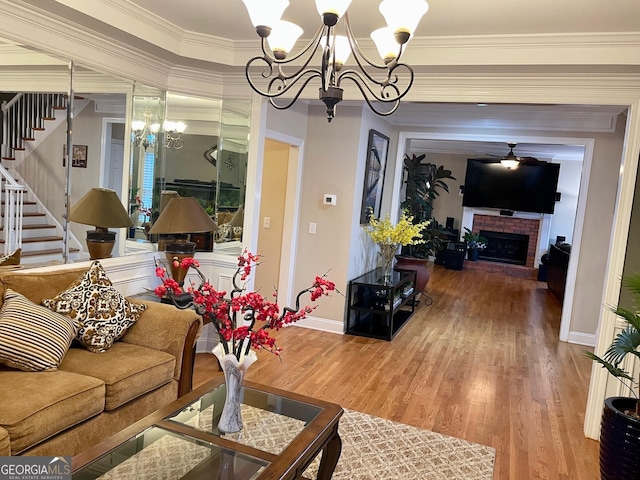 living room with ornamental molding, wood-type flooring, a notable chandelier, and a brick fireplace