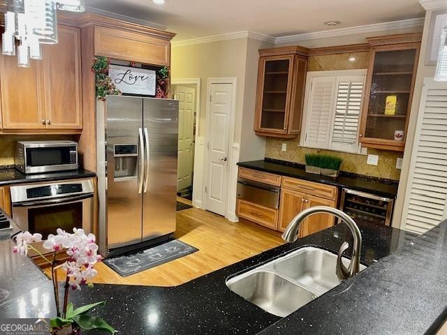 kitchen with light wood-type flooring, backsplash, ornamental molding, stainless steel appliances, and sink