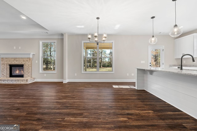 unfurnished living room featuring a healthy amount of sunlight, a brick fireplace, and dark wood-type flooring