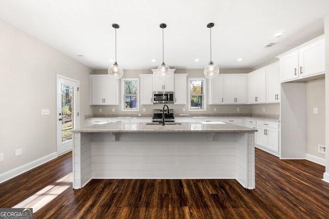 kitchen featuring appliances with stainless steel finishes, light stone counters, a center island with sink, dark hardwood / wood-style floors, and white cabinetry