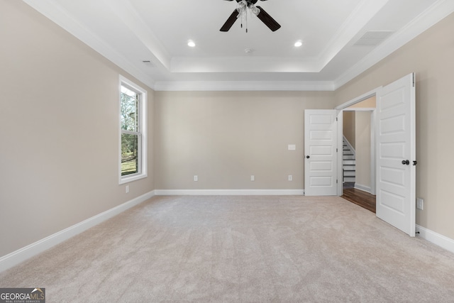 unfurnished bedroom featuring ceiling fan, ornamental molding, light carpet, and a tray ceiling