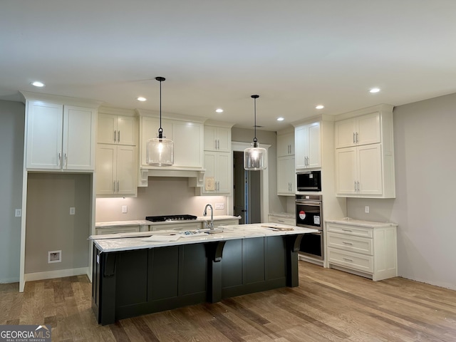 kitchen with pendant lighting, white cabinetry, light hardwood / wood-style flooring, and a kitchen island with sink