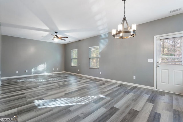 empty room with ceiling fan with notable chandelier, visible vents, baseboards, and wood finished floors