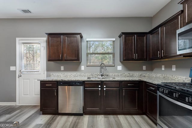 kitchen with stainless steel appliances, a sink, dark brown cabinets, a wealth of natural light, and light stone countertops