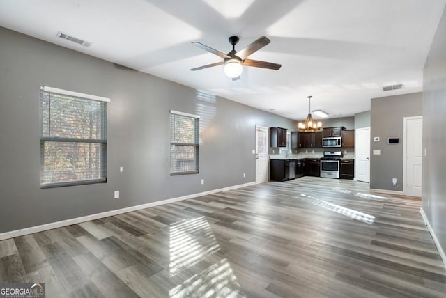 unfurnished living room with baseboards, visible vents, wood finished floors, and ceiling fan with notable chandelier