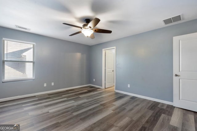 unfurnished room with dark wood-type flooring, visible vents, ceiling fan, and baseboards