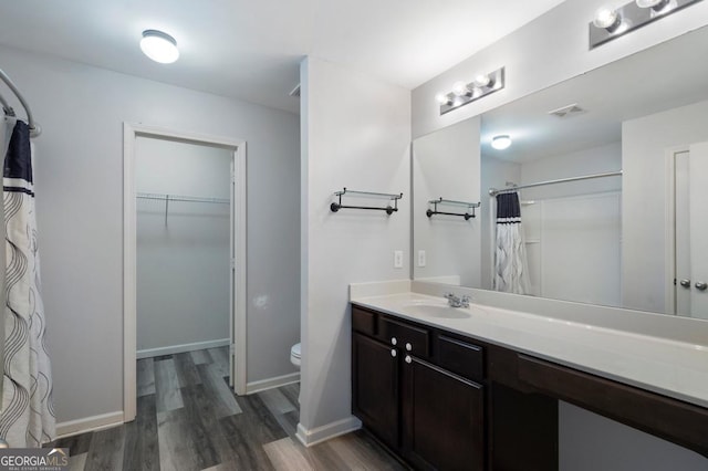 bathroom featuring baseboards, toilet, wood finished floors, a walk in closet, and vanity