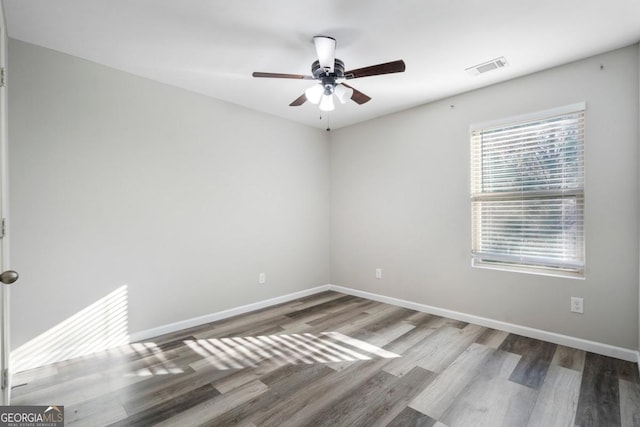 empty room with visible vents, wood finished floors, a ceiling fan, and baseboards