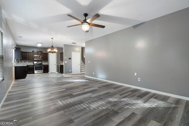 unfurnished living room with ceiling fan with notable chandelier, dark wood-type flooring, a sink, baseboards, and stairs