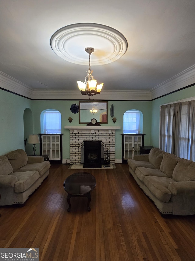 living room with crown molding, dark wood-type flooring, a notable chandelier, and a brick fireplace