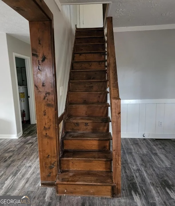 staircase with wood-type flooring, a textured ceiling, gas water heater, and ornamental molding