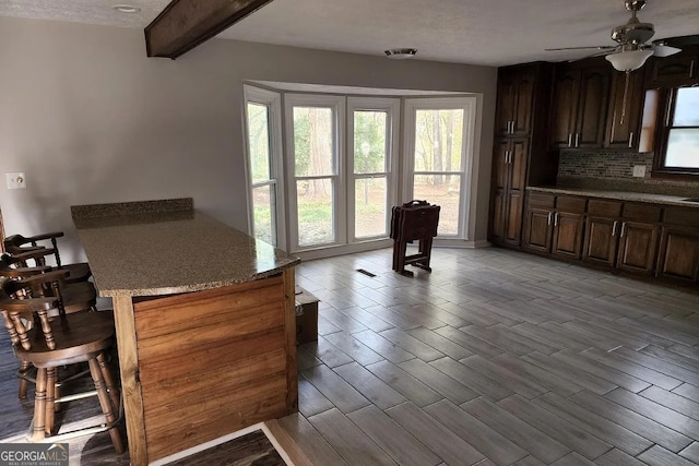 kitchen featuring light hardwood / wood-style flooring, ceiling fan, a textured ceiling, beam ceiling, and light stone counters