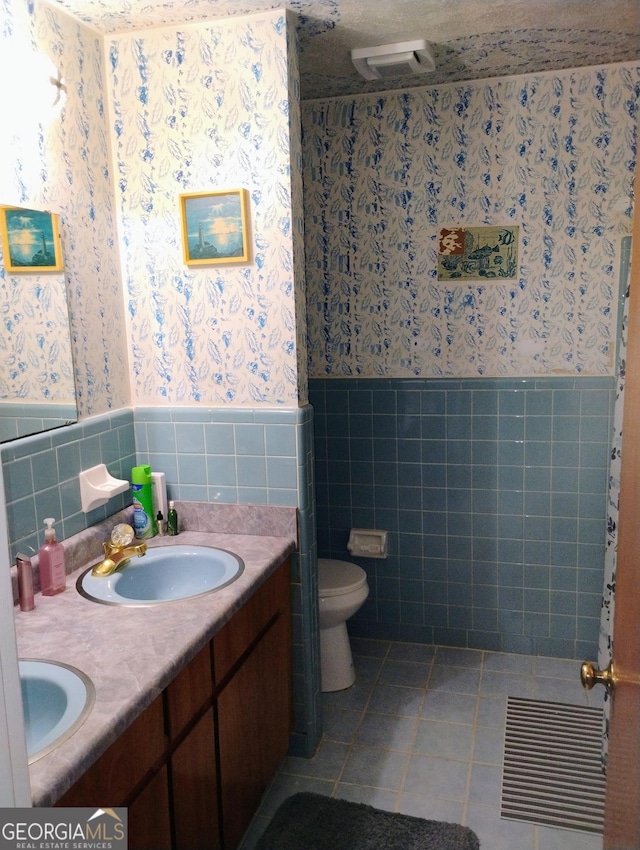 bathroom with tile patterned flooring, vanity, toilet, and tile walls