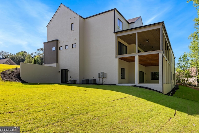 back of property featuring ceiling fan, a lawn, a sunroom, cooling unit, and stucco siding