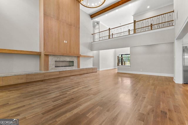 unfurnished living room featuring a towering ceiling, wood finished floors, beamed ceiling, a tiled fireplace, and a notable chandelier
