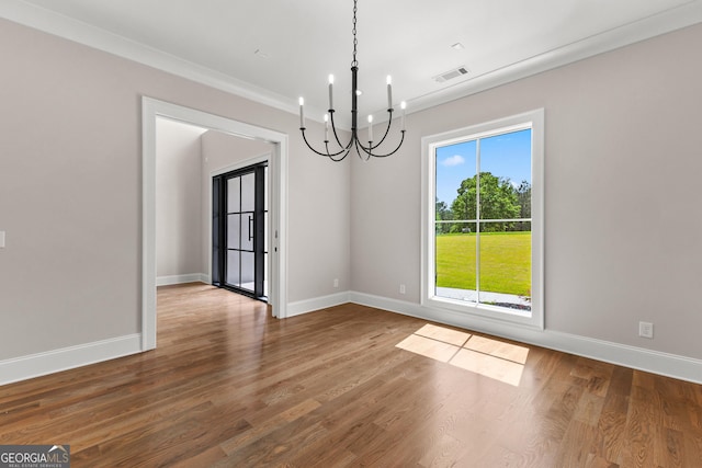 unfurnished dining area with an inviting chandelier, ornamental molding, visible vents, wood finished floors, and baseboards