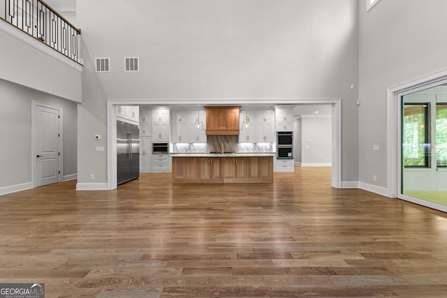 unfurnished living room featuring baseboards, visible vents, wood finished floors, and a towering ceiling