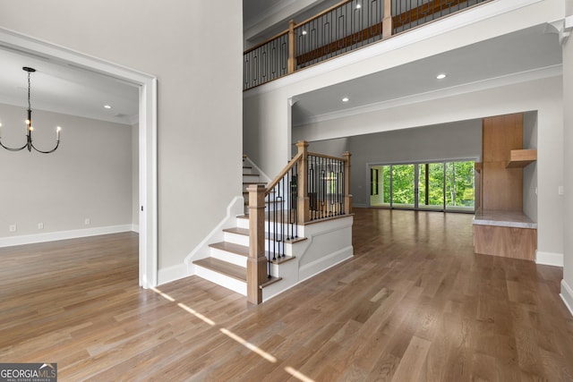 staircase featuring a notable chandelier, baseboards, wood finished floors, a towering ceiling, and ornamental molding