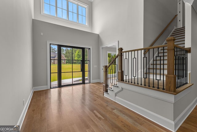 entryway featuring stairs, a towering ceiling, wood finished floors, and a wealth of natural light