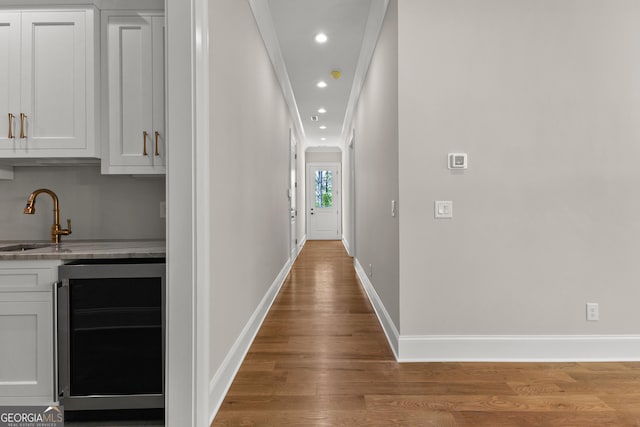 hall with a sink, recessed lighting, baseboards, wood finished floors, and wine cooler