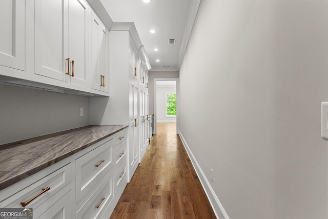 hallway featuring dark wood-style flooring, visible vents, baseboards, ornamental molding, and recessed lighting