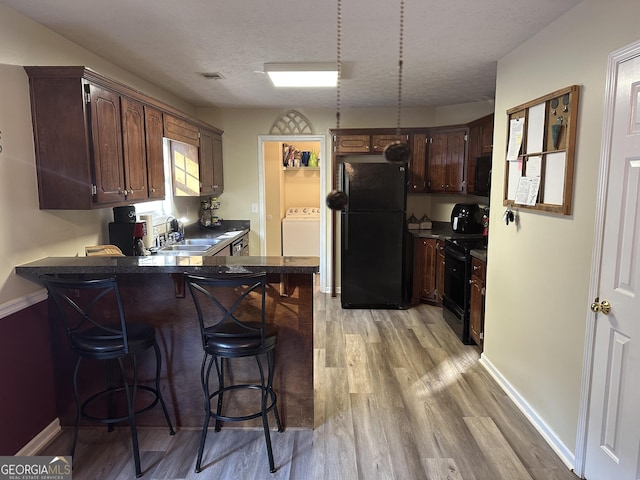 kitchen with black appliances, sink, dark brown cabinets, light hardwood / wood-style floors, and washer / clothes dryer