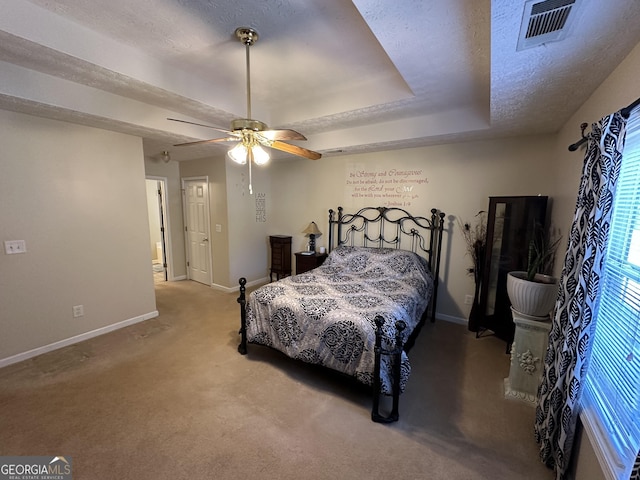 bedroom with a textured ceiling, light colored carpet, ceiling fan, and a tray ceiling