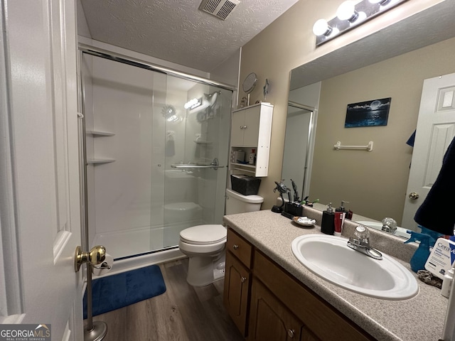 bathroom featuring vanity, a textured ceiling, a shower with door, wood-type flooring, and toilet