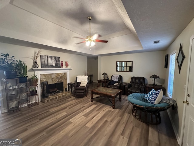 living room with a tray ceiling, ceiling fan, hardwood / wood-style floors, and a textured ceiling