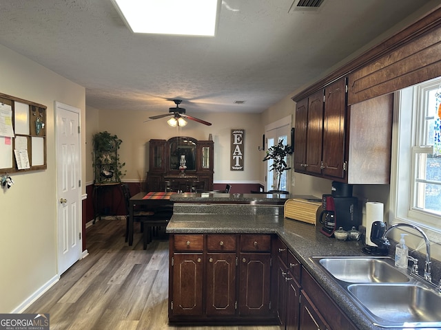 kitchen with a textured ceiling, dark brown cabinets, sink, and light hardwood / wood-style flooring