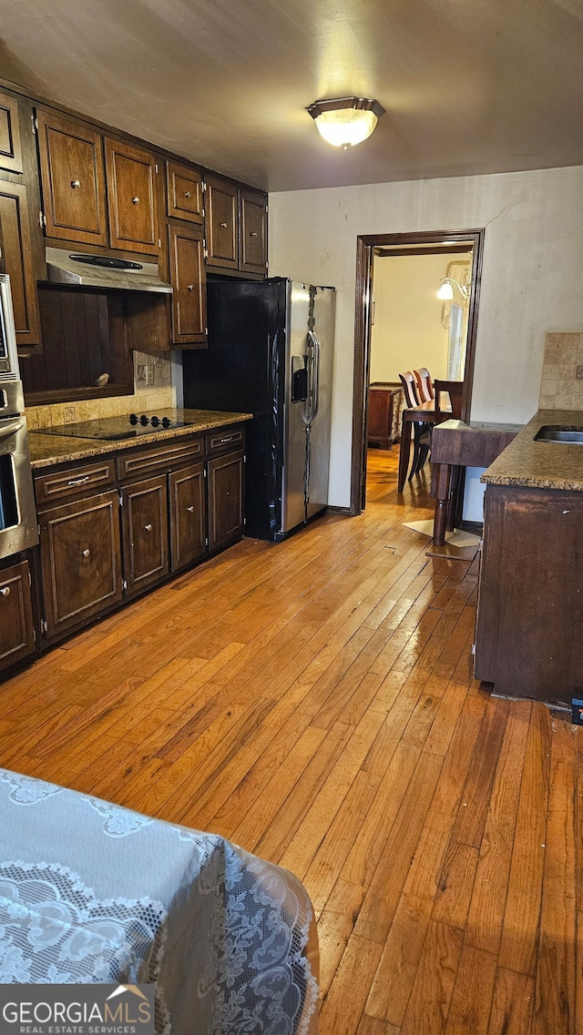 kitchen featuring appliances with stainless steel finishes, sink, backsplash, dark brown cabinets, and light wood-type flooring