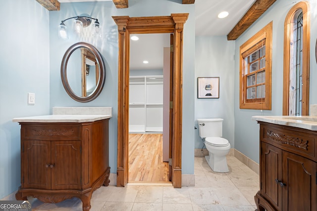 bathroom featuring beamed ceiling, vanity, wood-type flooring, and toilet