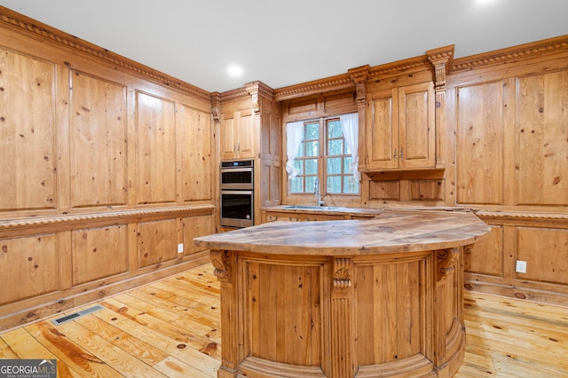 kitchen featuring wood counters, double oven, wood walls, light hardwood / wood-style floors, and a kitchen island