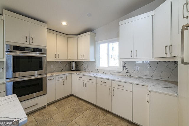 kitchen with backsplash, light stone counters, double oven, white cabinetry, and lofted ceiling