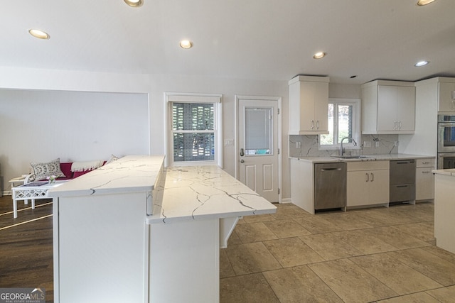 kitchen featuring white cabinets, sink, a kitchen island, light stone counters, and stainless steel appliances