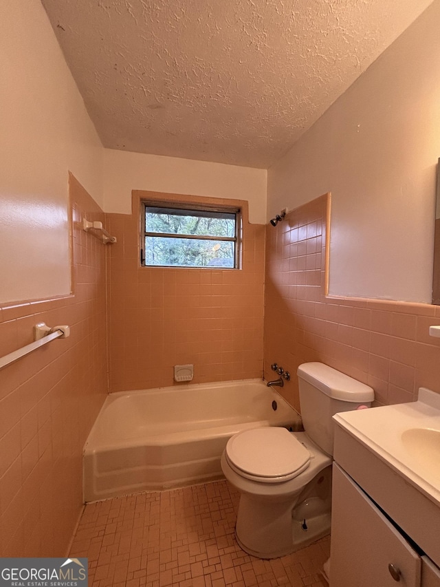 full bathroom featuring toilet, tile walls, a textured ceiling, vanity, and tiled shower / bath combo